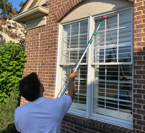 window cleaning professional in white shirt cleaning windows on brick home