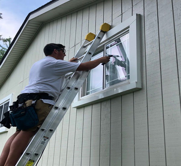 window cleaning professional on ladder cleaning window on white home